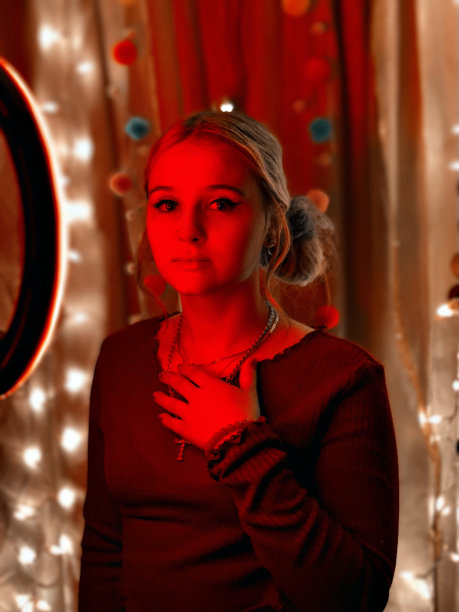 一个美丽的年轻女子的肖像在一个自制的照相亭聚会与红色照明。图片下载