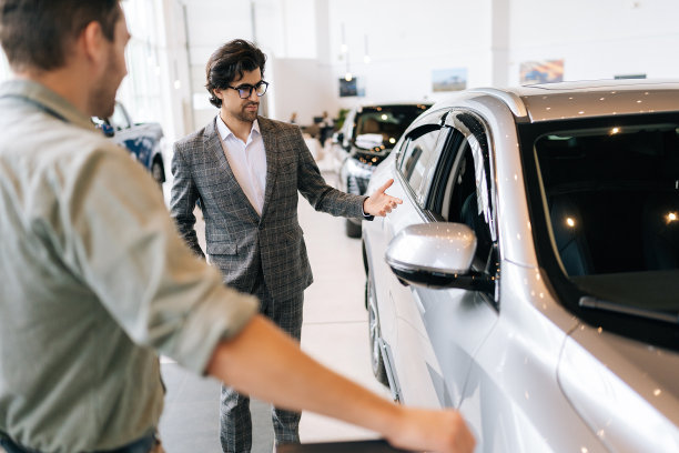 一幅穿着西装的汽车经销商的画像，他在经销商办公室里向一位无法辨认的沉思的男性买家讲述豪车。年轻男性客户的后视图图片下载