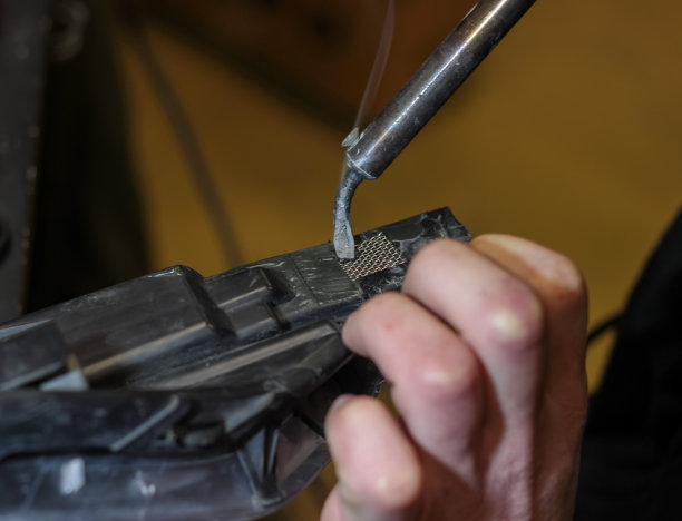 一名男子正在修复汽车车身的塑料。这个人手里拿着一个烙铁，用它来焊接零件。机械师用烙铁修理汽车。图片下载