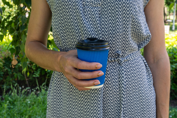 蓝色的咖啡纸杯在一个女孩的手中，在大自然的背景下，绿草图片下载