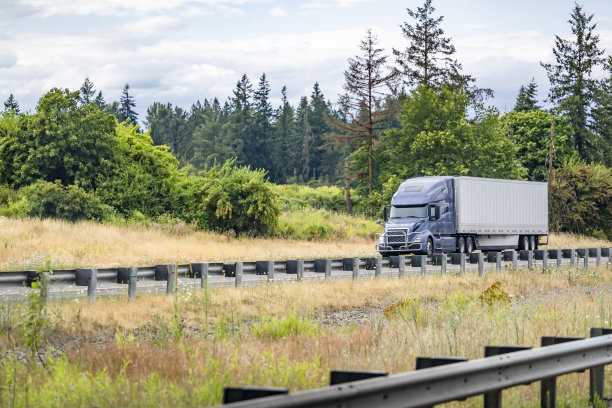 带格栅护栏的灰色大钻机半挂车，用干式货车半挂车运输货物，行驶在分隔的单向公路上，夏日景观图片下载