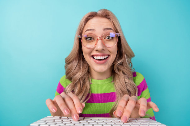 照片中，可爱的女人穿着条纹运动衫，在蓝绿色背景的键盘上发短信图片下载