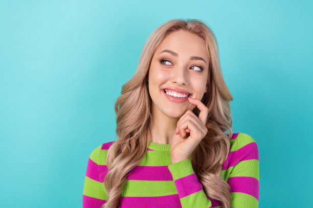 照片的头脑的女人卷曲的发型穿着条纹运动衫看起来空白的空间手指在牙齿孤立的蓝绿色背景图片下载