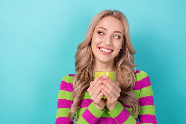 开朗的女人的照片，卷发，穿着条纹运动衫，拿着一杯浓咖啡，在蓝绿色的背景上看起来空无一物图片下载
