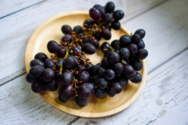 一张俯视图照片显示，一串串的黑葡萄排列在一个木制餐盘上。图片下载