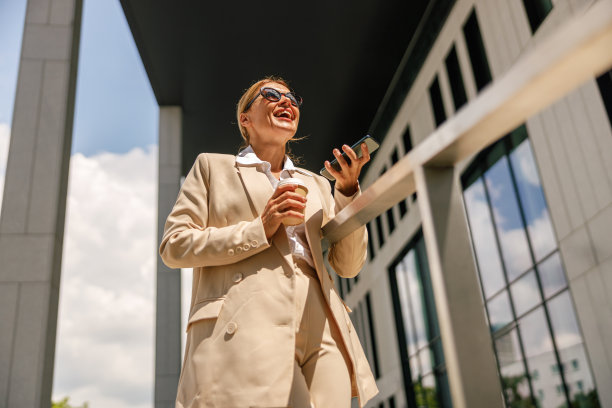 时尚的商务女性拿着手机站在现代建筑的背景下，端着咖啡图片下载