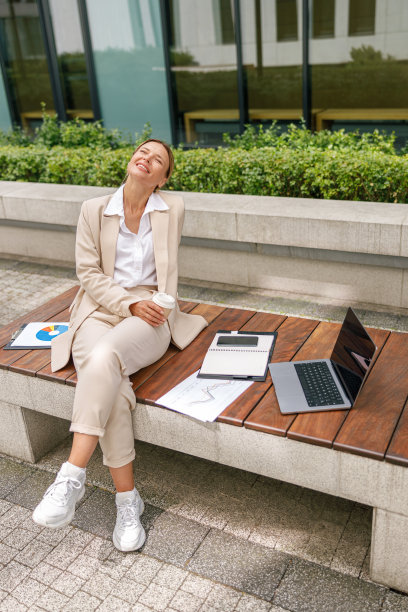 在办公大楼附近的休息时间，微笑的女商人坐在长凳上喝咖啡图片下载