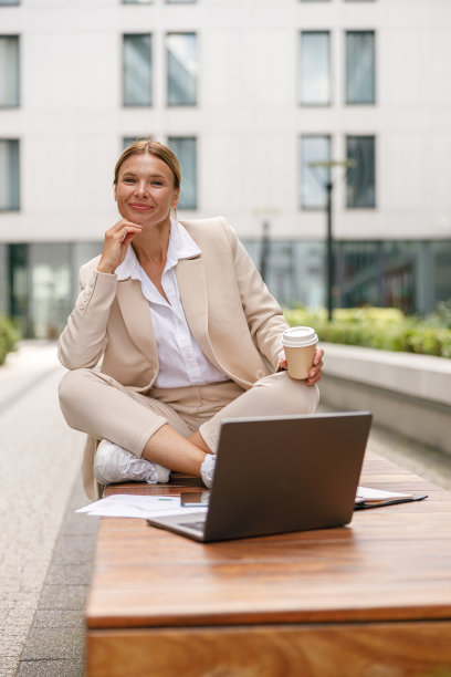女企业家坐在长凳上用笔记本电脑工作，在办公室的背景下喝咖啡图片下载