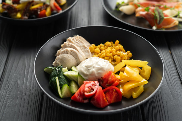 鸡肉健康午餐。鸡肉片和蔬菜沙拉，玉米，西红柿，黄瓜和奶油在黑暗的桌子。生酮饮食食谱。图片下载