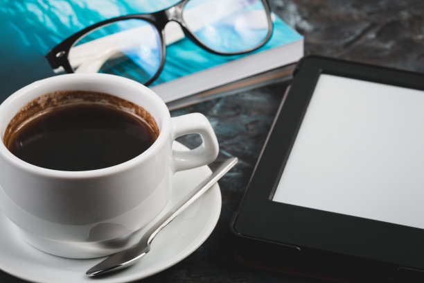 桌上有电子书和纸质书，还有一杯咖啡，一台笔记本电脑和老花镜。自我教育的概念。图片下载