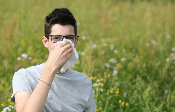 戴眼镜的男孩在户外对着白手帕打喷嚏，因为他对花粉过敏图片下载