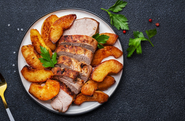 烤猪里脊配甜榅桲或苹果片，白色盘子。黑色表格背景，俯视图图片下载