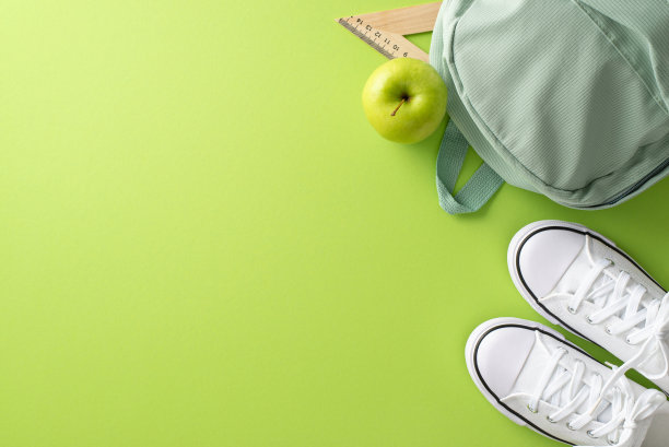 用这张视觉上令人惊叹的俯视图照片吸引你的观众，照片上有一个背包、运动鞋、水果和文具，背景是浅绿色的。非常适合教育活动和广告图片下载