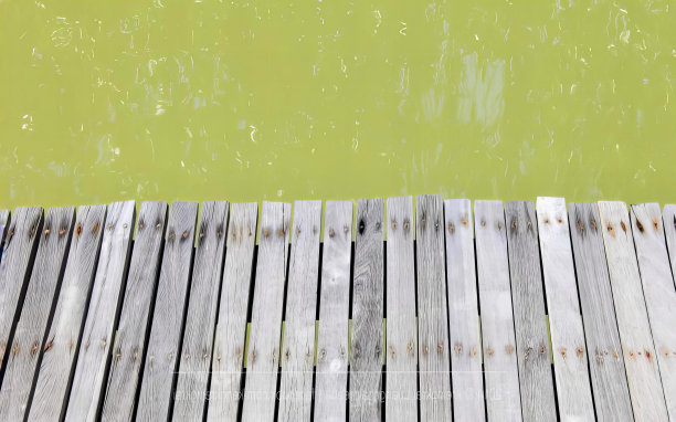 一张以绿水为背景的木码头的照片，有一个木码头，绿色的水和黄色的船。图片下载