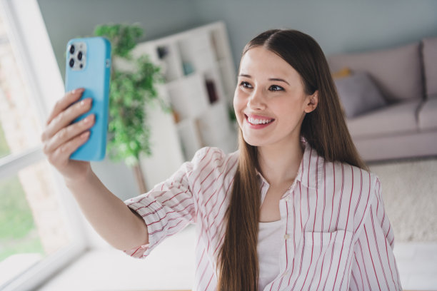 照片肖像迷人的年轻女子手持小工具照片自拍谈话穿着时尚智能休闲服装室内舒适的房间家庭办公室图片下载