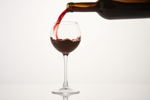 圆波状的粉红色葡萄酒从瓶颈流向玻璃杯。图片下载