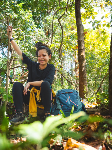 徒步旅行一天后，一个背着大背包的妇女在森林里的原木上休息。图片下载