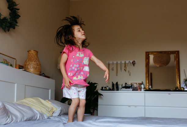 小孩子穿着粉红色的睡衣，头发扎得高高的，在父母的床上跳来跳去图片下载