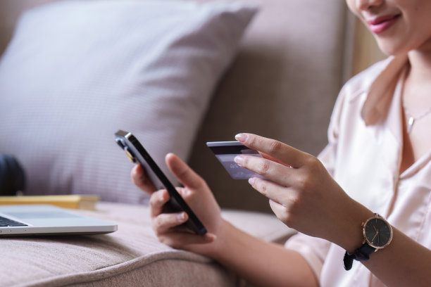 漂亮的亚洲女人坐在家里的沙发上用信用卡和智能手机在网上购物图片下载