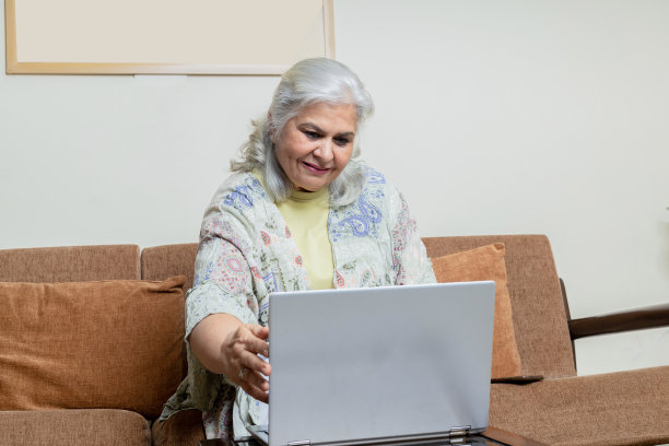 印度资深女性使用笔记本电脑，对着笔记本电脑微笑图片下载
