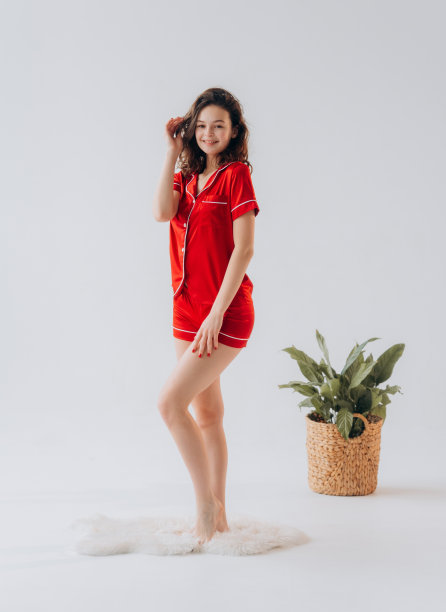 穿着红色睡衣的开朗年轻女子站在室内，背景是白色。图片下载