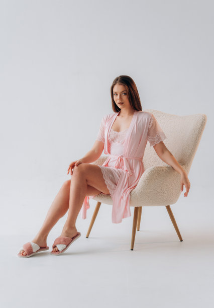 穿着粉色丝绸睡衣的女孩坐在白色工作室背景的扶手椅上图片下载