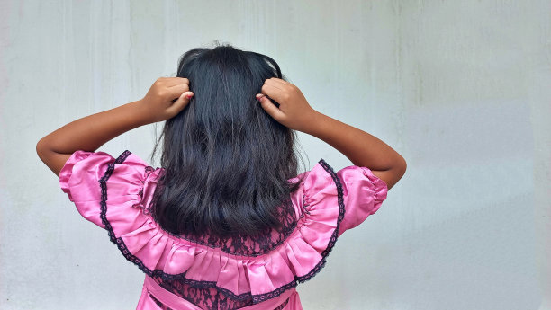 后视图的小女孩穿着粉红色的聪明的休闲裙布抱着头。长头发的小学生图片下载