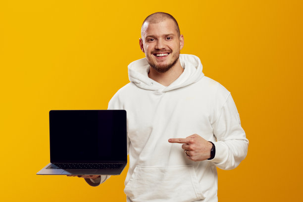 穿着白色连帽衫的年轻男孩微笑着用手指着黄色背景上的电脑图片下载