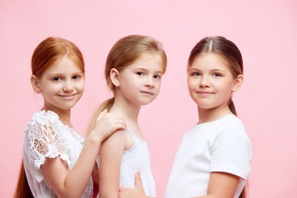 三个穿着白色衣服，扎着马尾辫的小女孩在粉色演播室背景前的肖像图片下载