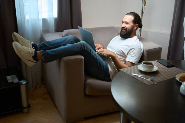 酒店客人穿着休闲服，坐在舒适的椅子上，手里拿着笔记本电脑图片下载