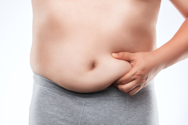 一个穿着灰色内衣的胖子露出腹部和大腿上的脂肪堆积。营养不合理的观念，久坐的生活方式。超重的治疗。图片下载