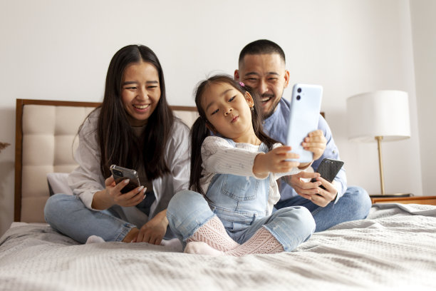 亚洲家庭坐在床上通过视频通话交流，韩国小女孩和爸爸妈妈自拍图片下载