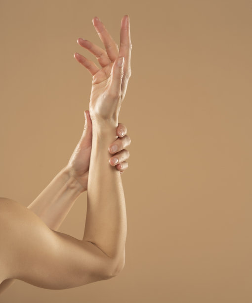 在米色背景上，一名女子在手上涂抹化妆品。年轻女子在涂护手霜图片下载