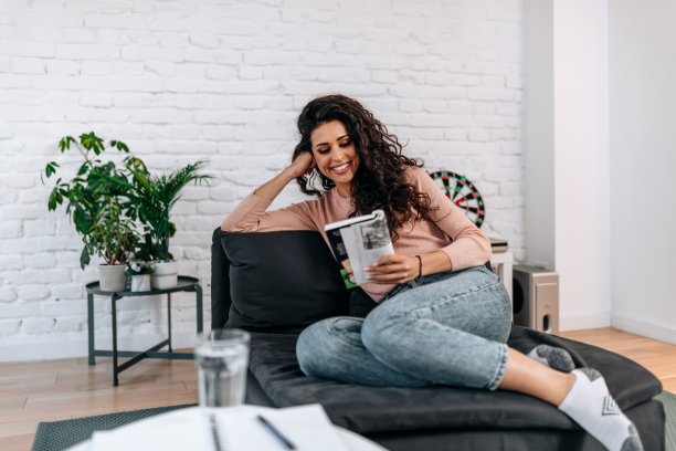 年轻女子坐在舒适的扶手椅和打开的书在室内。图片下载