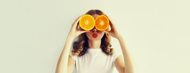 夏天，营养，饮食和素食的概念。快乐、健康、开朗的年轻女子用橙色水果片蒙住眼睛，寻找白色背景上的东西图片下载