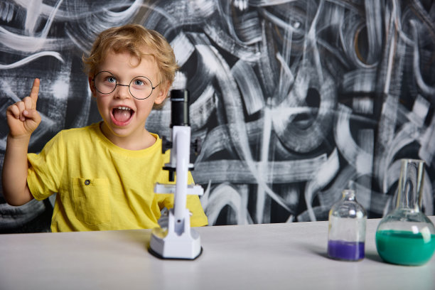 一个戴圆眼镜、身穿黄色t恤的好奇男孩在显微镜下看到了一种微生物图片下载