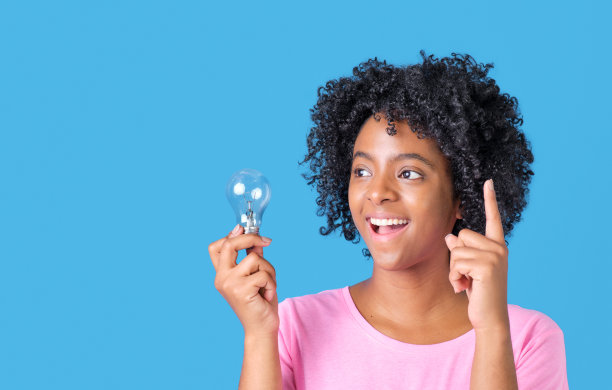 非裔美国女孩微笑着，手里拿着灯泡，穿着蓝色背景的粉色t恤图片下载