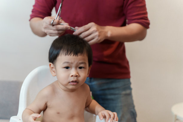 可爱的父亲在家里给他的宝贝儿子理发。微笑的可爱小男孩第一次被他的爸爸剪头发。图片下载