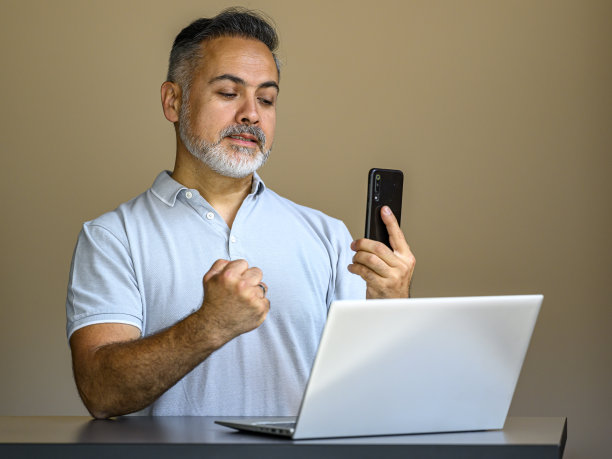 一个失望的商人拿着笔记本电脑看着他的手机图片下载