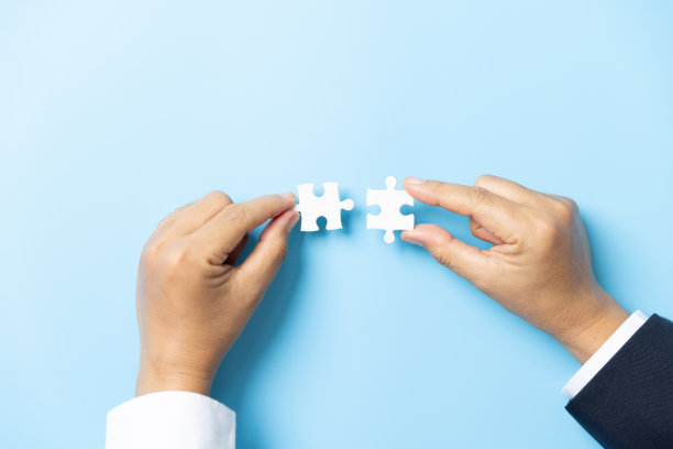 两只手试图在蓝色背景上连接一对拼图。团队合作的概念。连接拼图的特写手。图片下载