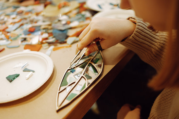 女性在制作马赛克时用镊子夹住玻璃片的手的特写。图片下载