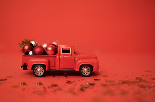 红色玩具卡车，后备箱里有圣诞球和冷杉树枝。红色背景圣诞装饰的微型汽车。明亮的背景与火花和五彩纸屑。图片下载