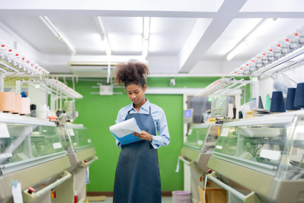 美国女设计师、织布工站在纺织工厂的房间中间，拿着一张单子检查产品订单图片下载