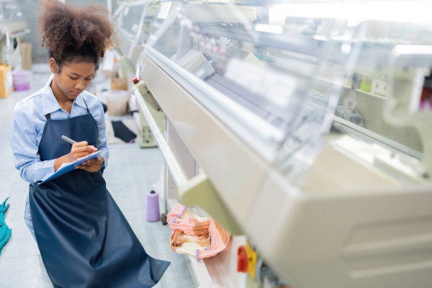 美国女设计师、织女的特写，坐下来记下产品设计订单的清单。有一台缝纫机在工作。在一个庞大的织造工业中图片下载