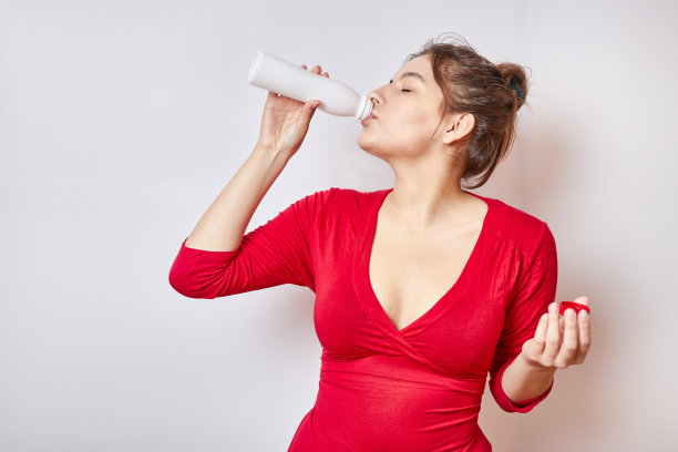 穿着红衬衫的漂亮女孩正在用瓶子喝饮料。图片下载