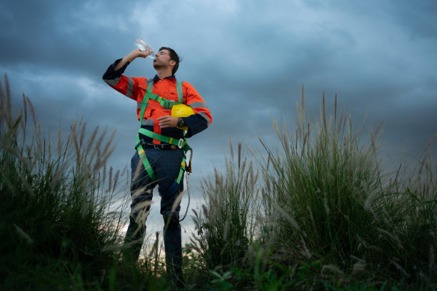 一个年轻人的肖像，在风力发电机领域工作，穿着安全背心，下班后放松时间的概念图片下载