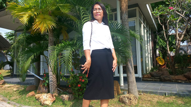 一个亚洲女人穿着漂亮的休闲装，拿着细绳钱包站在房子或办公楼前的姿势图片下载