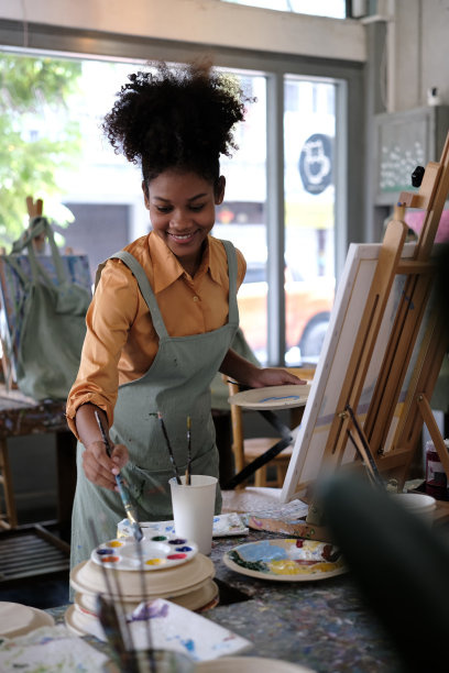 微笑的非裔美国女艺术家创作杰作，在艺术工作室用毛笔在画布上作画。图片下载
