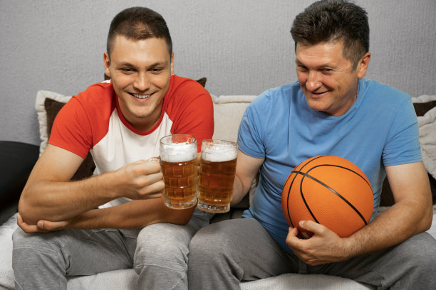 父亲和儿子在家里看篮球比赛，手里拿着一品脱啤酒图片下载