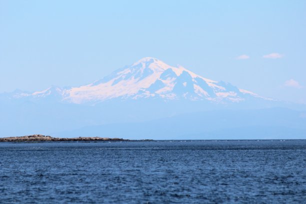 这是一张从乔治亚海峡俯瞰贝克山的令人难以置信的照片，背景是巨大的雪山，在前景中从海洋中升起。图片下载